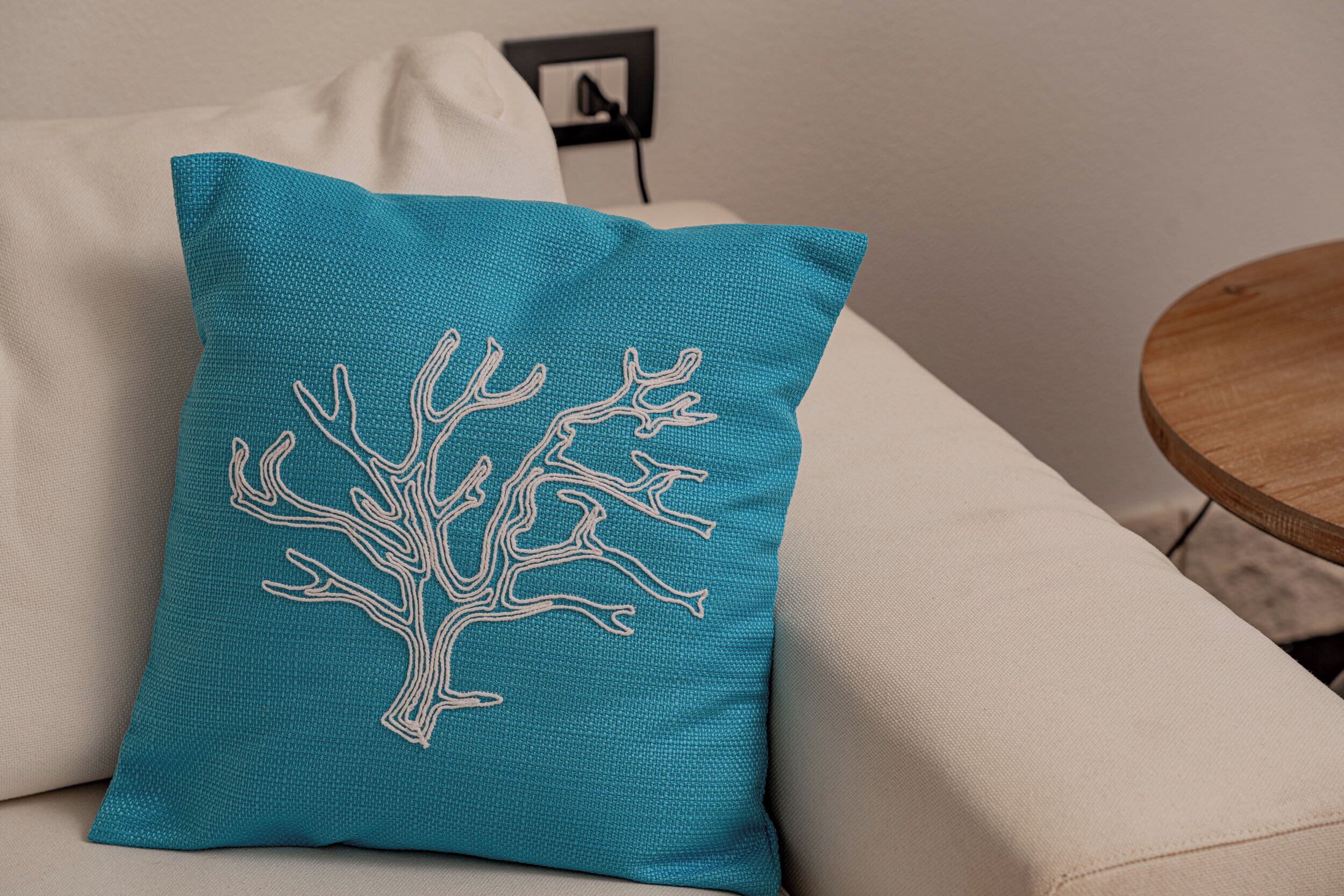 A teal pillow with a tree design on a beige sofa.