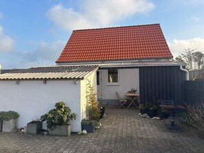 A house with a red-tiled roof, a small patio with a table and chairs, and several potted plants. - 4 Person Holiday Home in Hanstholm (Hanstholm)