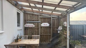A covered patio with a wooden table and chairs, a grill, and directional signs for 'Rengoring' and 'Vask'. - 4 Person Holiday Home in Hanstholm (Hanstholm)