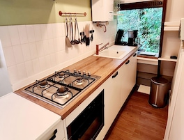 Una cocina con estufa a gas, gabinetes blancos, una ventana con vistas a la vegetación y una cafetera.