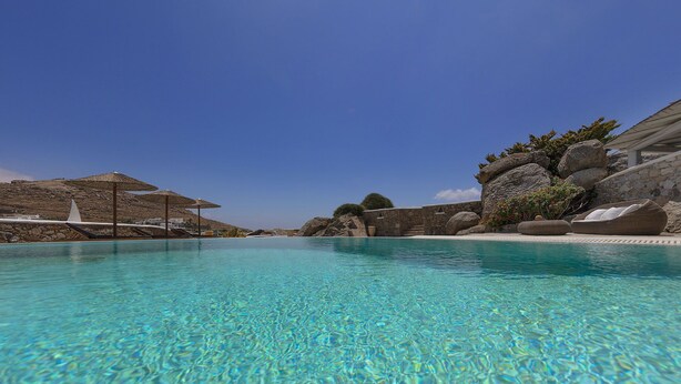 A clear blue pool with lounge chairs and umbrellas, surrounded by rocky terrain and a clear sky. - My Rental Homes - Villa Cassandra, less than 2 km from the beach with pool (Mykonos)