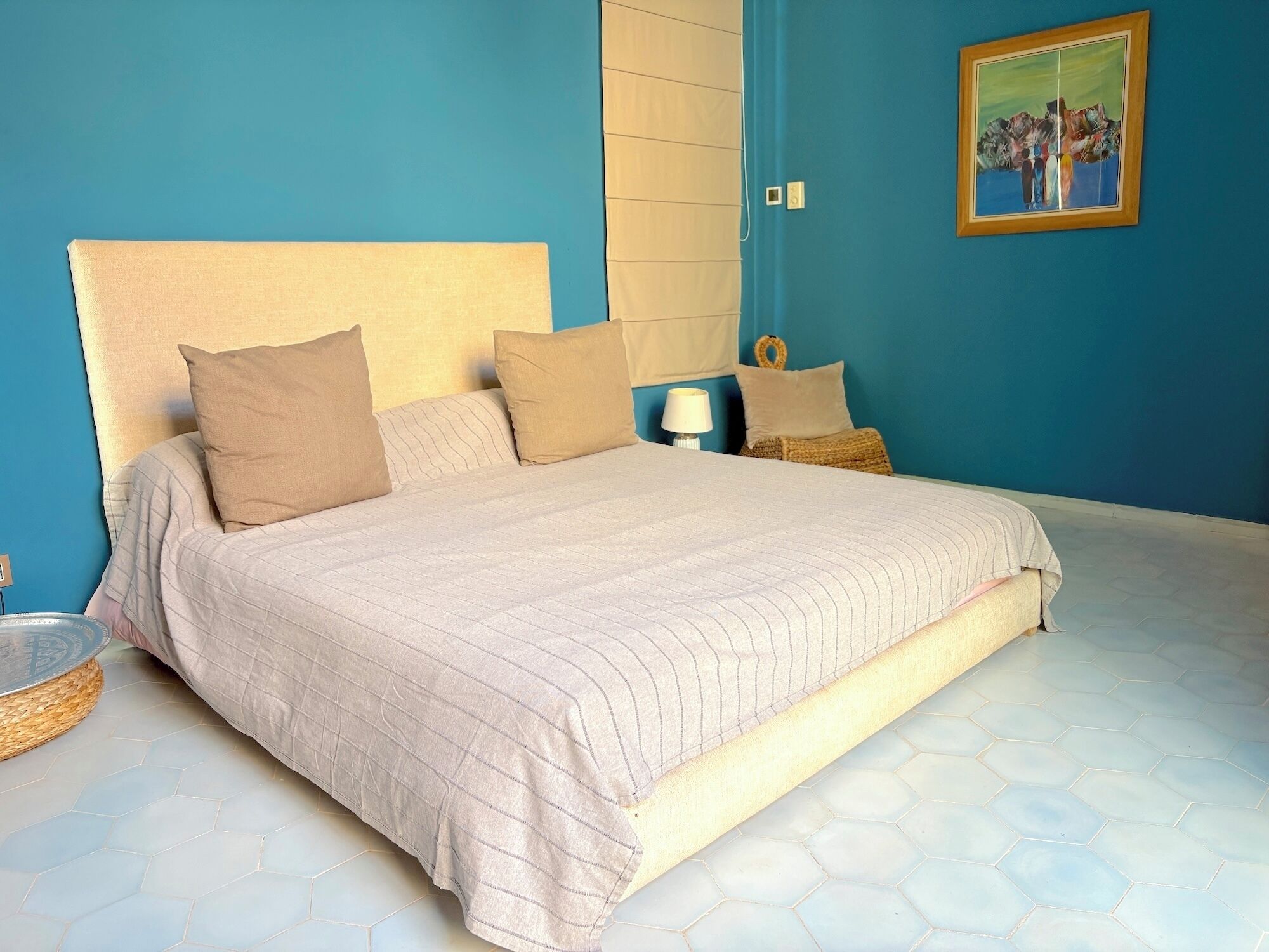 A bedroom with a large bed, a headboard, and a painting on the wall.