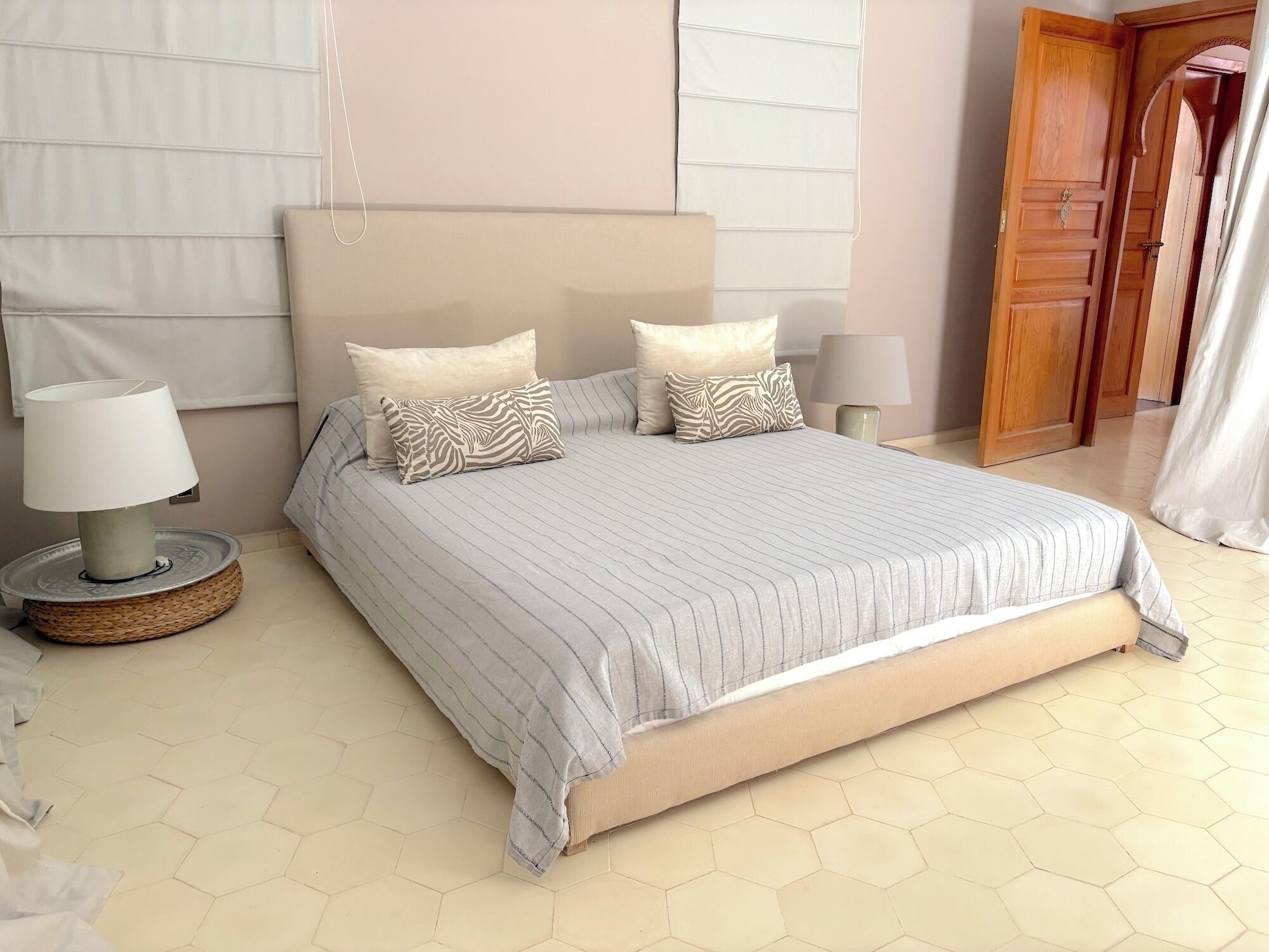 A neatly made bed with striped bedding and two pillows, a bedside lamp, and a woven bedside table.