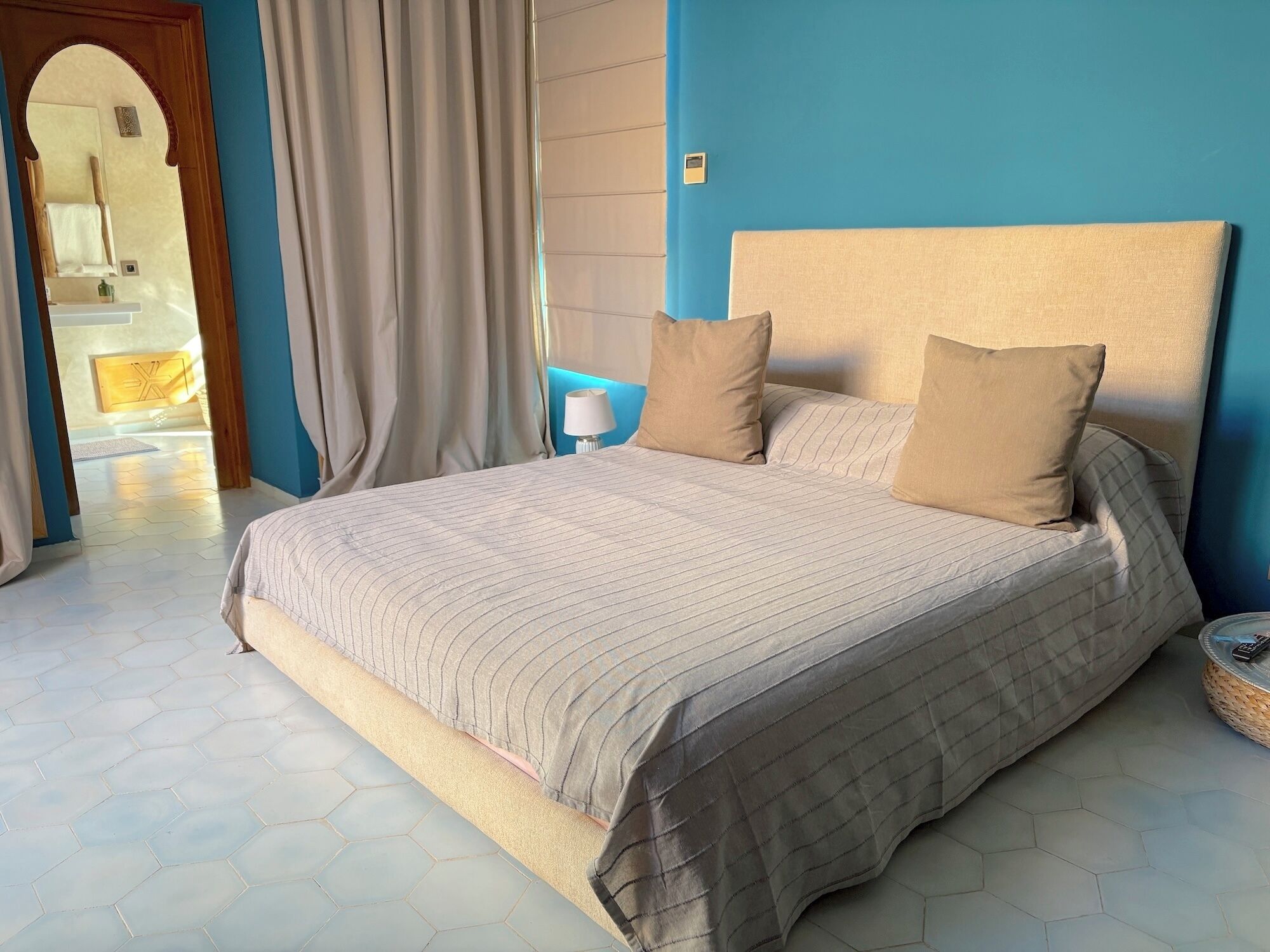 Ein Schlafzimmer mit einem großen Bett, zwei Kissen, einer Nachttischlampe und einem Blick ins Bad durch einen Bogen.