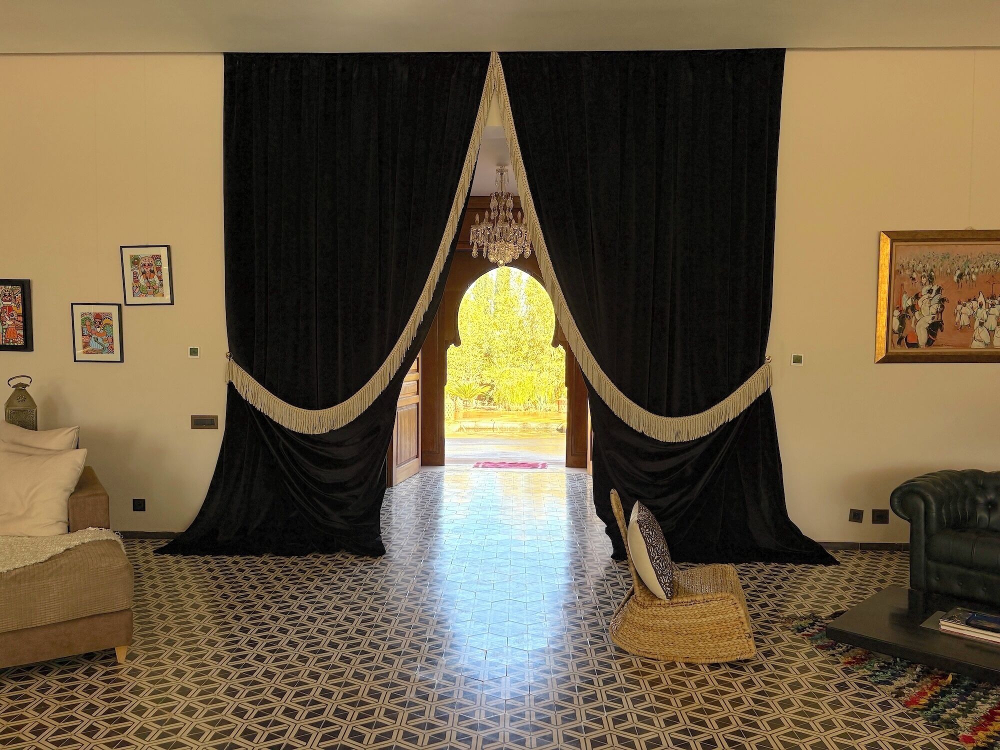 Une pièce avec un sol à motifs, un canapé, un fauteuil et une grande fenêtre ornée de rideaux noirs.