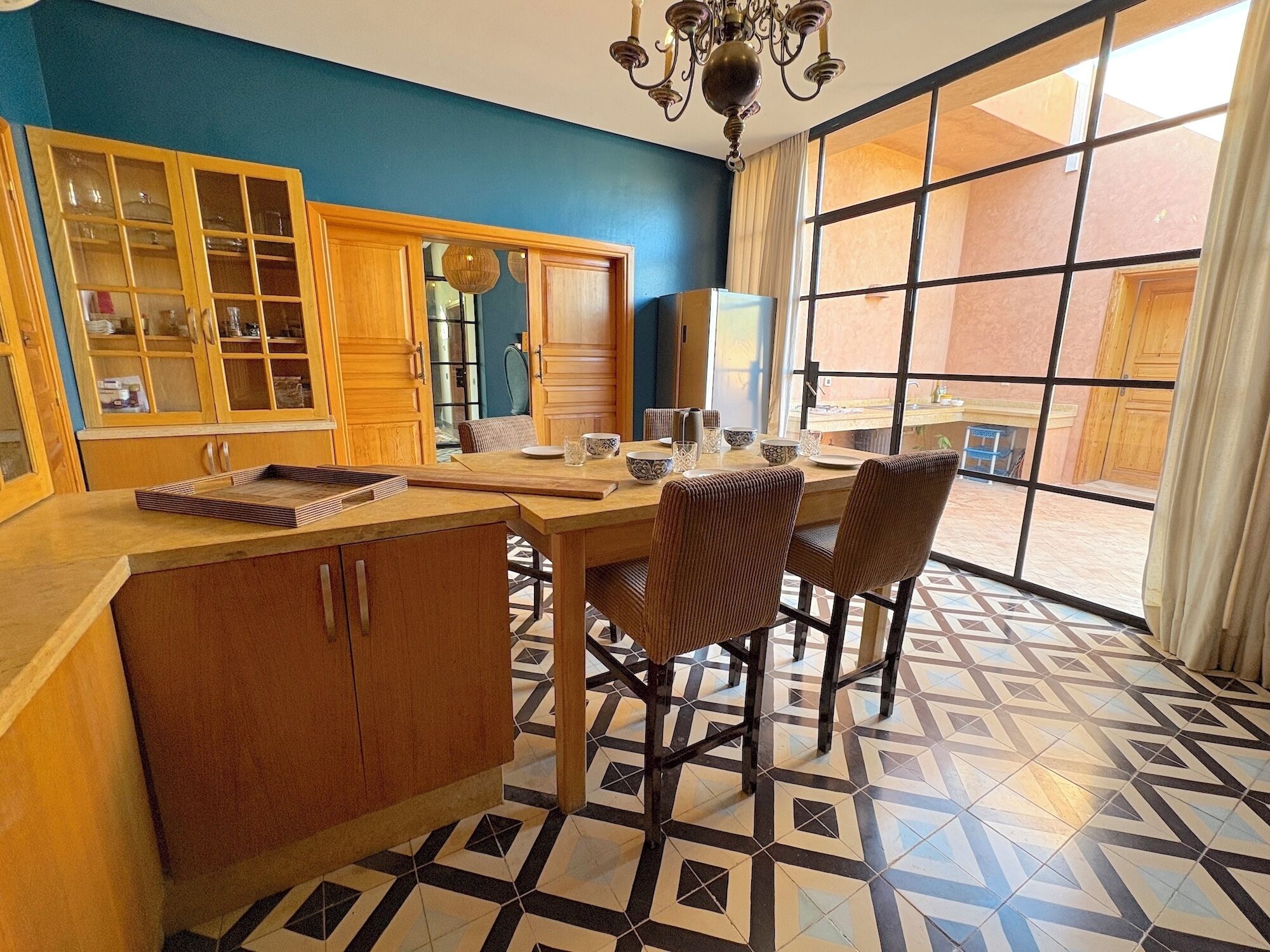 Un espace repas avec une table et des chaises en bois, un lustre et une vue dégagée grâce à de grandes fenêtres.