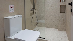 Uma casa de banho moderna com chuveiro em cabine de vidro, sanita branca e um aviso de não produzir lixo na parede.