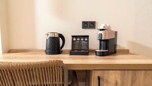 Uma secretária de madeira com uma cafeteira, um bule e uma caixa de cápsulas de café.