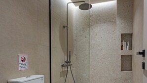 Casa de banho moderna com chuveiro em cabine de vidro, sanita branca e placa a proibir o descarte de lixo na sanita.
