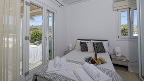 A bedroom with a bed, bedside tables, a window, and a view of the outdoors. - Panoramic Villa Fos, in Mykonos, in Kalafatis area, with private pool, 4 bedrooms, 10 sleeps (Mykonos)