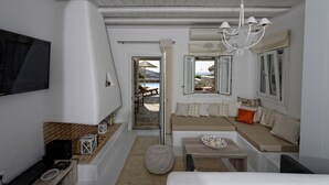 A modern living room with a sofa, a TV mounted on the wall, and a view of the outdoors. - Panoramic Villa Fos, in Mykonos, in Kalafatis area, with private pool, 4 bedrooms, 10 sleeps (Mykonos)