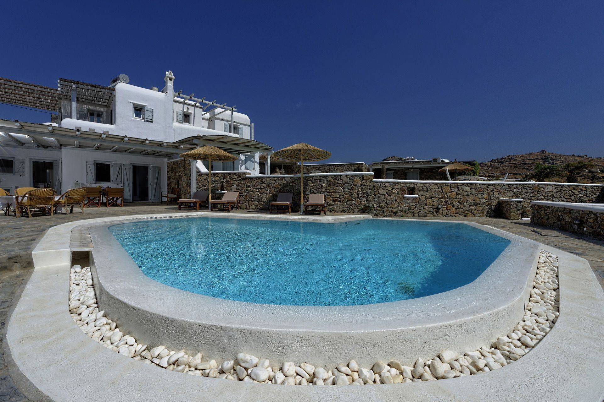 A pool with white pebbles, lounge chairs, and a stone wall.