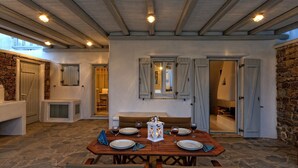 A dining area with a wooden table set for four, stone flooring, and a stone wall. - Panoramic Villa Fos, in Mykonos, in Kalafatis area, with private pool, 4 bedrooms, 10 sleeps (Mykonos)