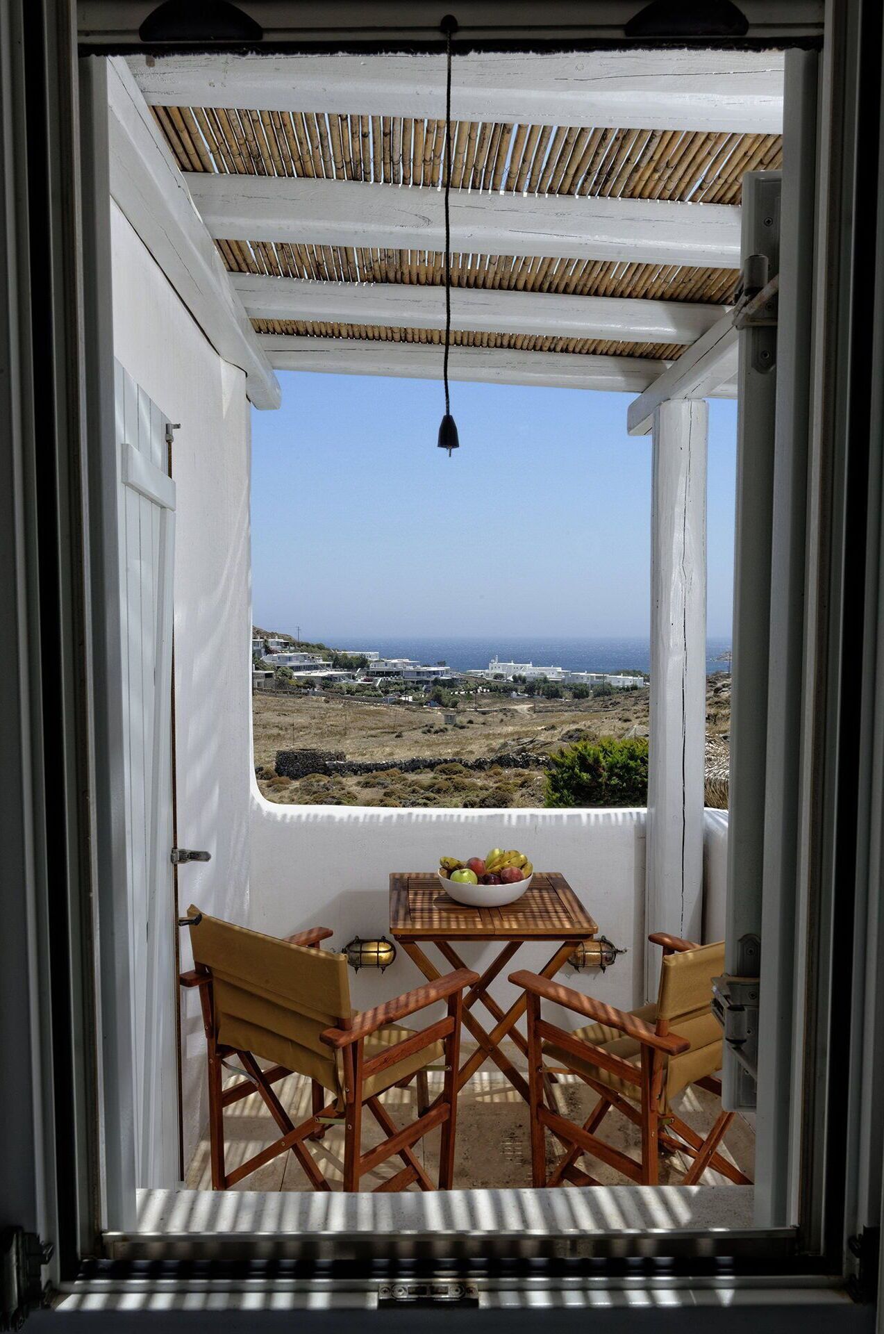 A balcony with a table and two chairs, overlooking a coastal landscape with buildings and the sea.