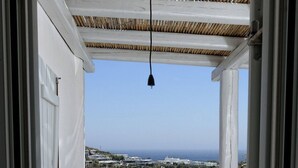 A balcony with a table and two chairs, overlooking a coastal landscape with buildings and the sea. - Panoramic Villa Fos, in Mykonos, in Kalafatis area, with private pool, 4 bedrooms, 10 sleeps (Mykonos)