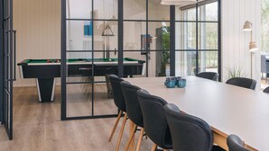 Una habitación moderna con mesa de billar, una mesa de comedor con sillas y un ventanal grande.