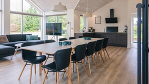 Una cocina moderna con una isla grande, un comedor con una mesa larga y sillas, y una sala de estar con sofá y televisor.