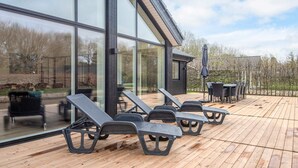 Una casa moderna con amplios ventanales, una terraza de madera y mobiliario exterior.