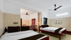 Habitación de hotel con dos camas, un ventilador de techo, una silla roja y una puerta que da a un baño.