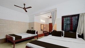 Habitación de hotel con dos camas individuales, una cama doble, ventilador de techo, ventana con cortinas y una silla.