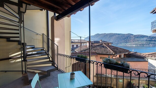Un balcon avec une table et des chaises, un escalier et une vue sur la mer et les bâtiments.