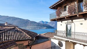 Un bâtiment doté d’un toit en tuiles, d’un balcon orné de plantes et offrant une vue sur un lac et des montagnes.