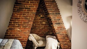 Une pièce avec un mur en briques incliné, une chaise blanche et un lit avec une literie à rayures.