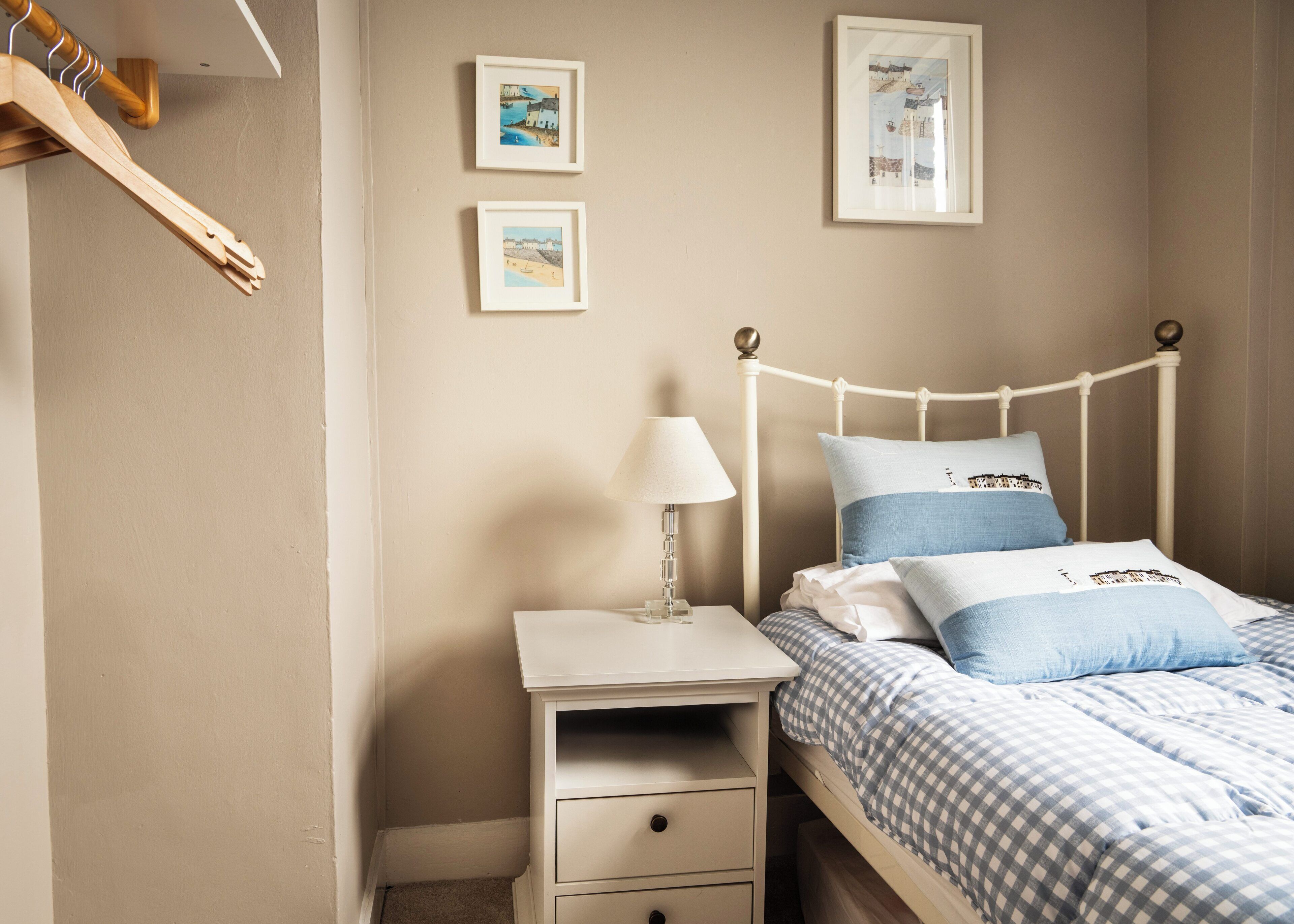 Quarto com cama, mesa de cabeceira, abajur e duas quadros na parede.