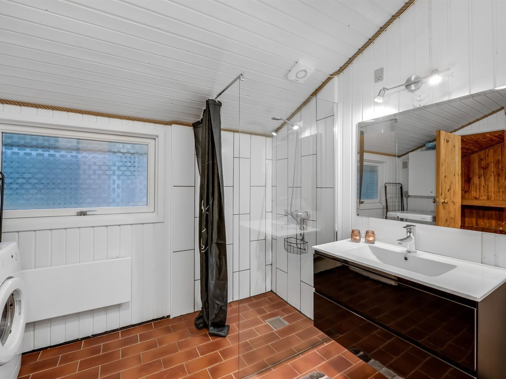Un baño con ventana, ducha, lavabo y espejo.