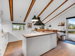 Eine moderne Küche mit einer zentralen Kochinsel, Holzbalken an der Decke und großen Fenstern.