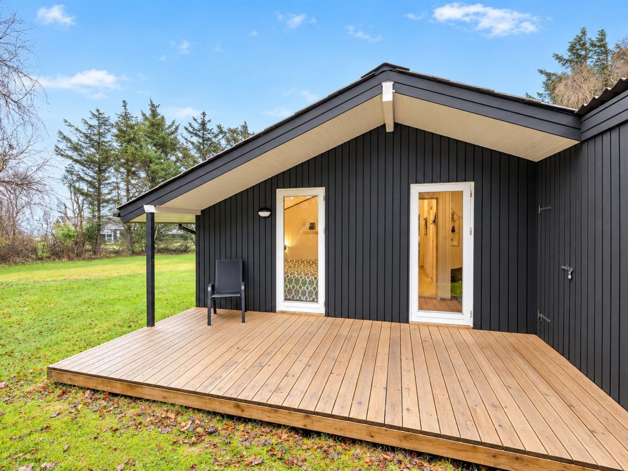 Une maison moderne dotée d’une terrasse en bois, d’une façade noire et d’une seule porte donnant sur un espace intérieur.
