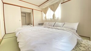 Ein ordentlich bezogenes Bett in einem Hotelzimmer mit einem großen Spiegel, einem Fenster mit Vorhängen und einer gemusterten Fußmatte.