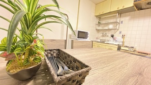 Cozinha equipada com micro-ondas, pia e fogão. Há uma planta em vaso e uma cesta com utensílios.