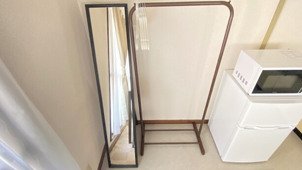 Ein kleines Zimmer mit Spiegel, Wäscheständer und einem weißen Gerät, vermutlich einer Mikrowelle.