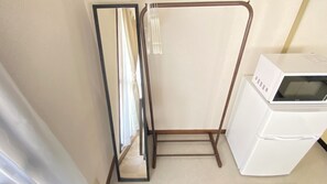 Ein kleines Zimmer mit Spiegel, Wäscheständer und einem weißen Gerät, vermutlich einer Mikrowelle.