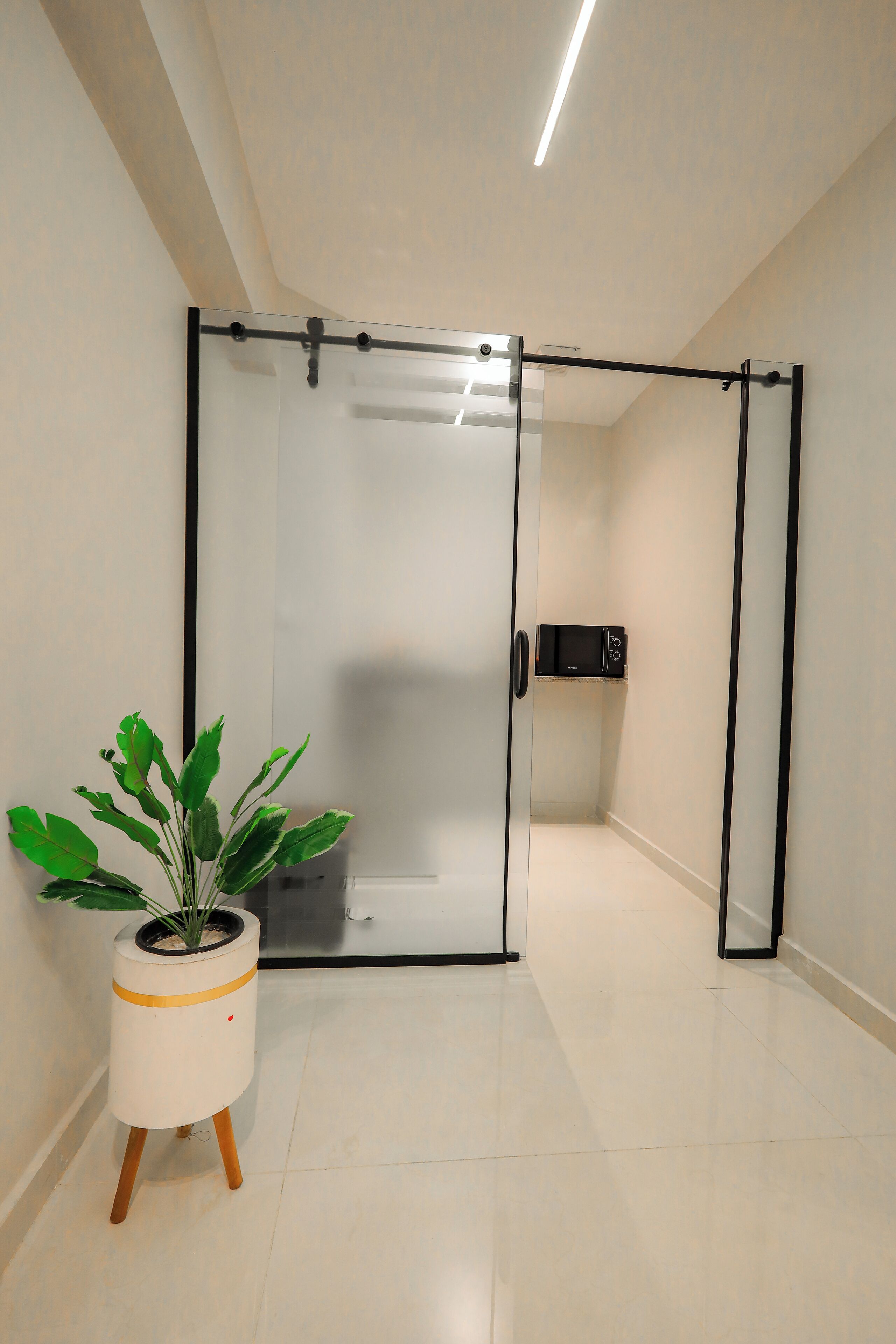 Une chambre moderne avec une porte-fenêtre coulissante, une plante en pot et un four à micro-ondes fixé au mur.