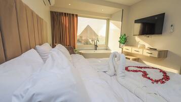 Une chambre d’hôtel avec un grand lit, une télévision, une fenêtre donnant sur une pyramide et une baignoire.