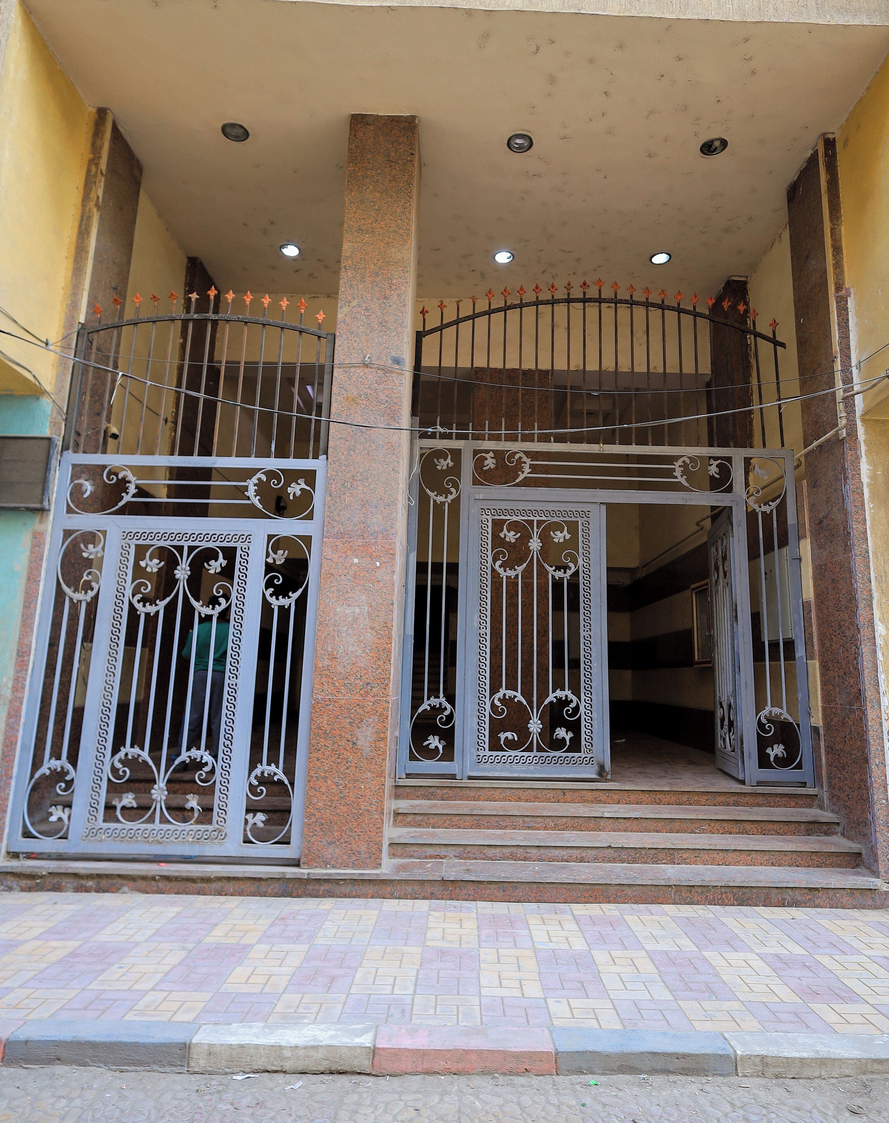 Une entrée d’immeuble avec un portail en métal, un escalier et un sol carrelé.