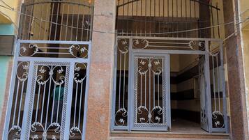 Une entrée d’immeuble avec un portail en métal, un escalier et un sol carrelé.