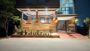 Un edificio moderno de dos pisos con techo plano, ventanas amplias y un área de entrada cubierta con plantas en macetas.
