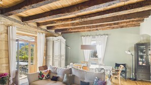 A cozy living room with a wooden ceiling, a sofa with cushions, a dining table, and a cabinet. - Valley View – Large house for 10 – Pool (Les Eyzies-de-Tayac-Sireuil)