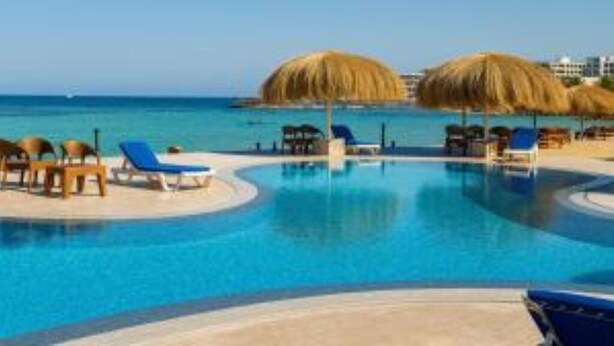 A pool area with lounge chairs and umbrellas, a clear blue pool, and a view of the sea. - Single Room with Sea View – Aquatic Village, Red Sea Resort (Red Sea Governorate)
