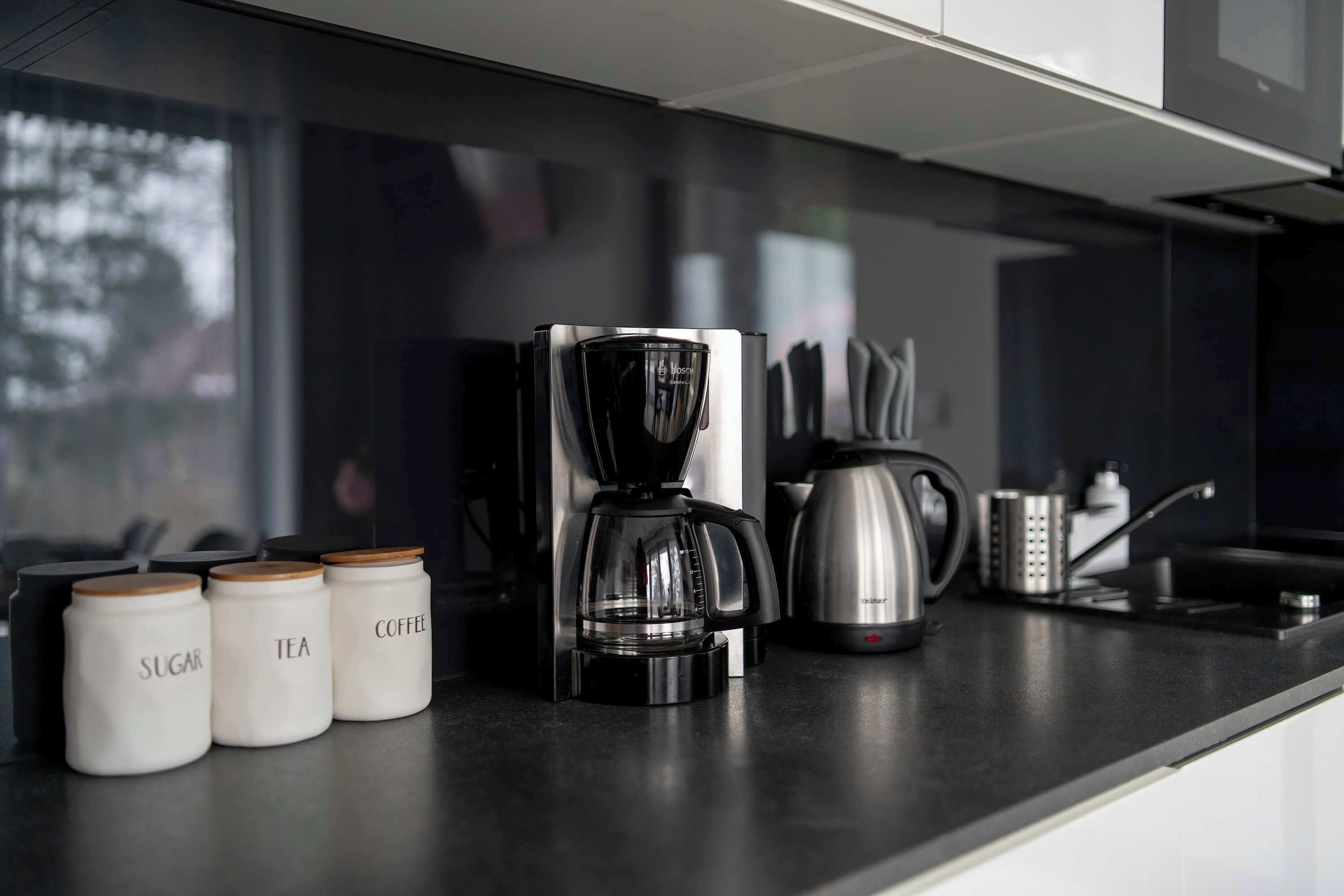 Een moderne keuken met een koffiezetapparaat, suiker, en bakken met thee en koffie op het aanrecht.