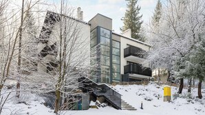 Moderni rakennus, jossa on lasijulkisivu, portaikko, joka johtaa parvekkeelle, ja lumipeitteiset puut.