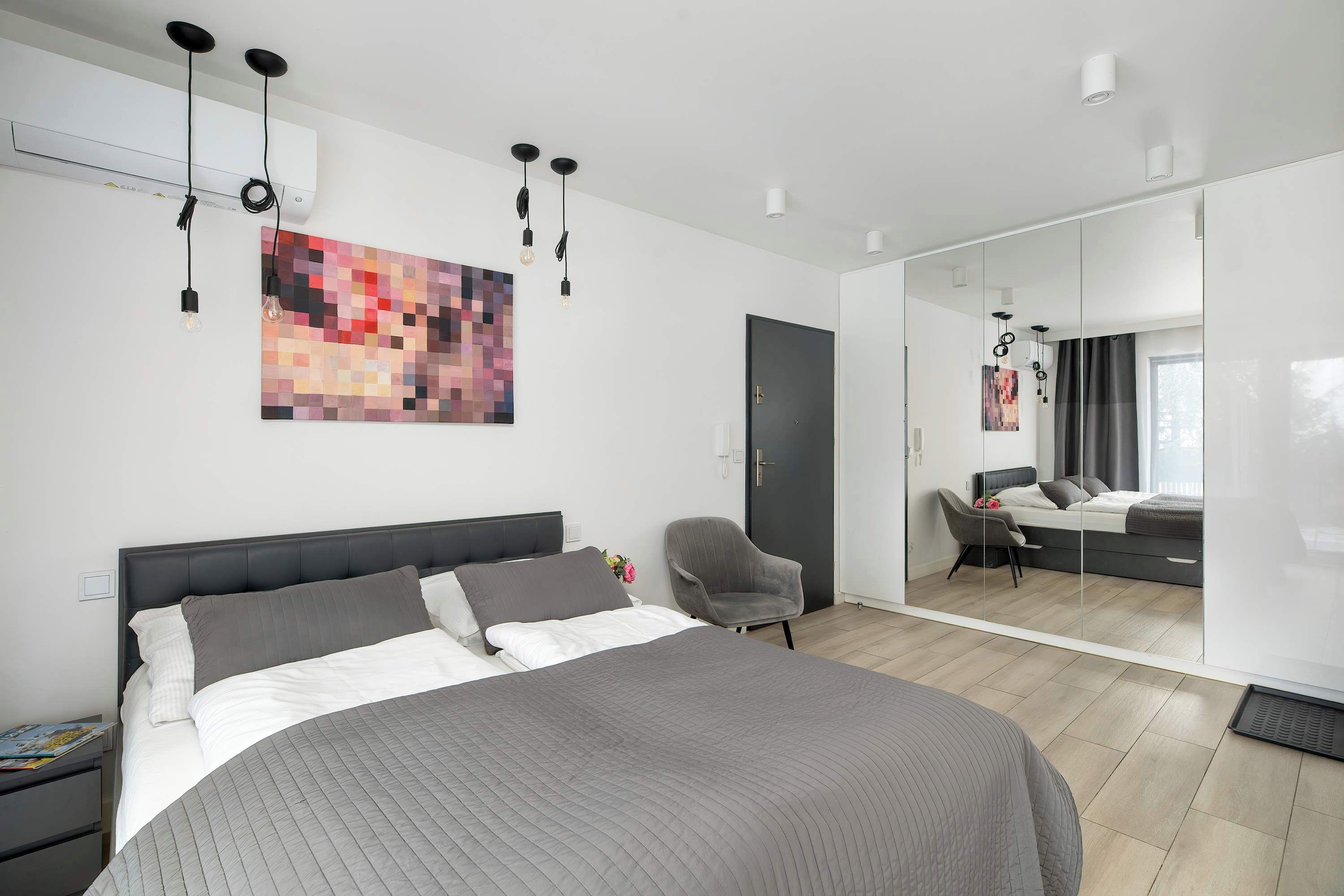 A modern hotel room with a large bed, a chair, a desk, and a mirror.