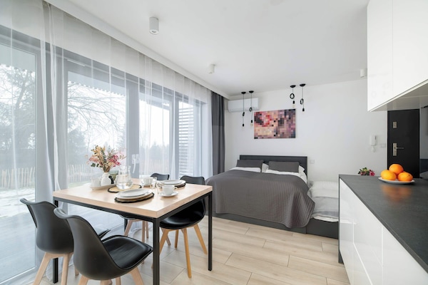 A bright dining and living area with large windows letting in natural light. A small table is set for a meal beside a cozy sitting space.