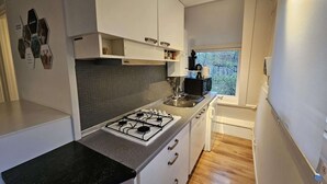 Una cocina moderna con armarios blancos, estufa a gas, lavamanos y ventana con vistas a árboles.