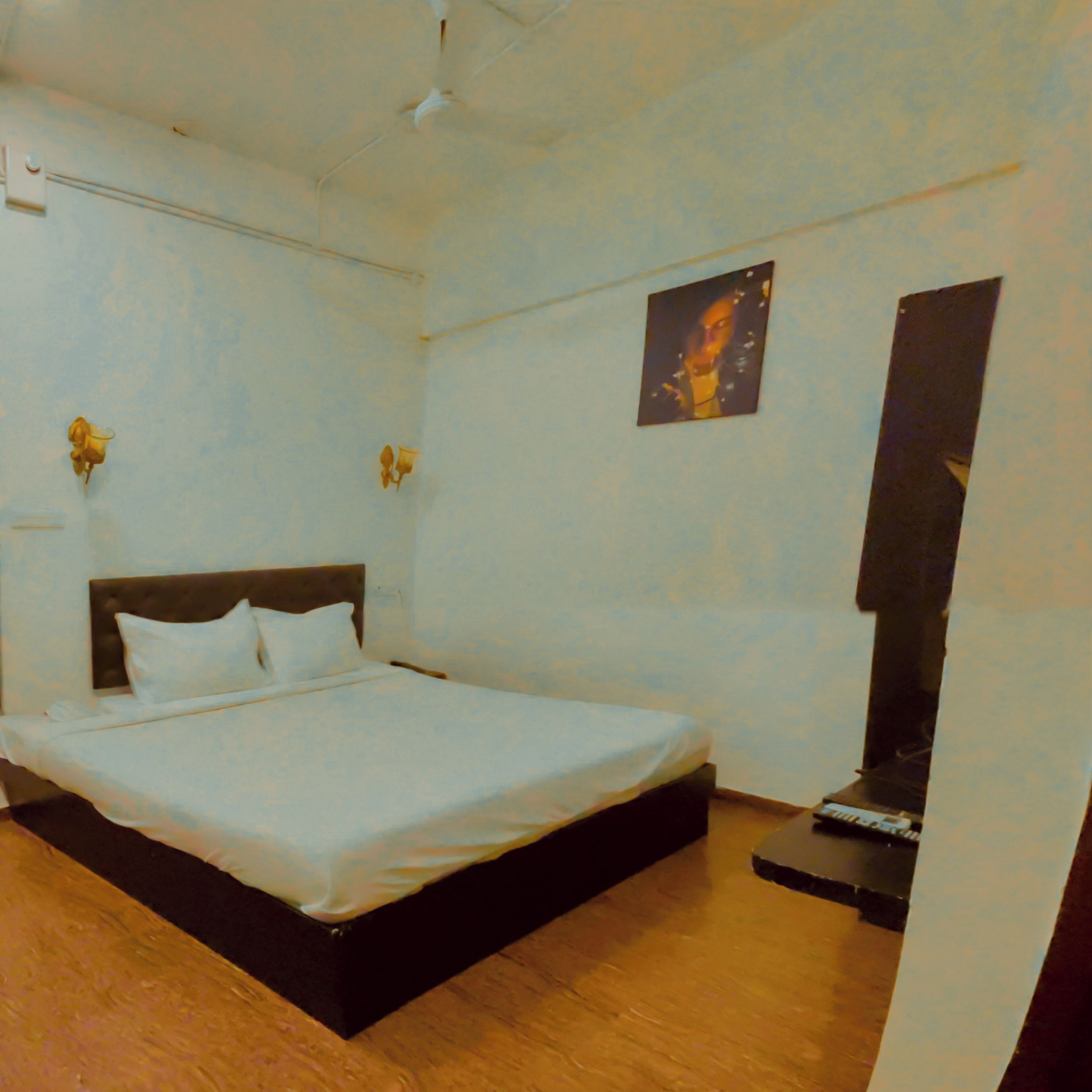 Una camera da letto con un letto, un comodino, una lampada a muro e un piccolo quadro.