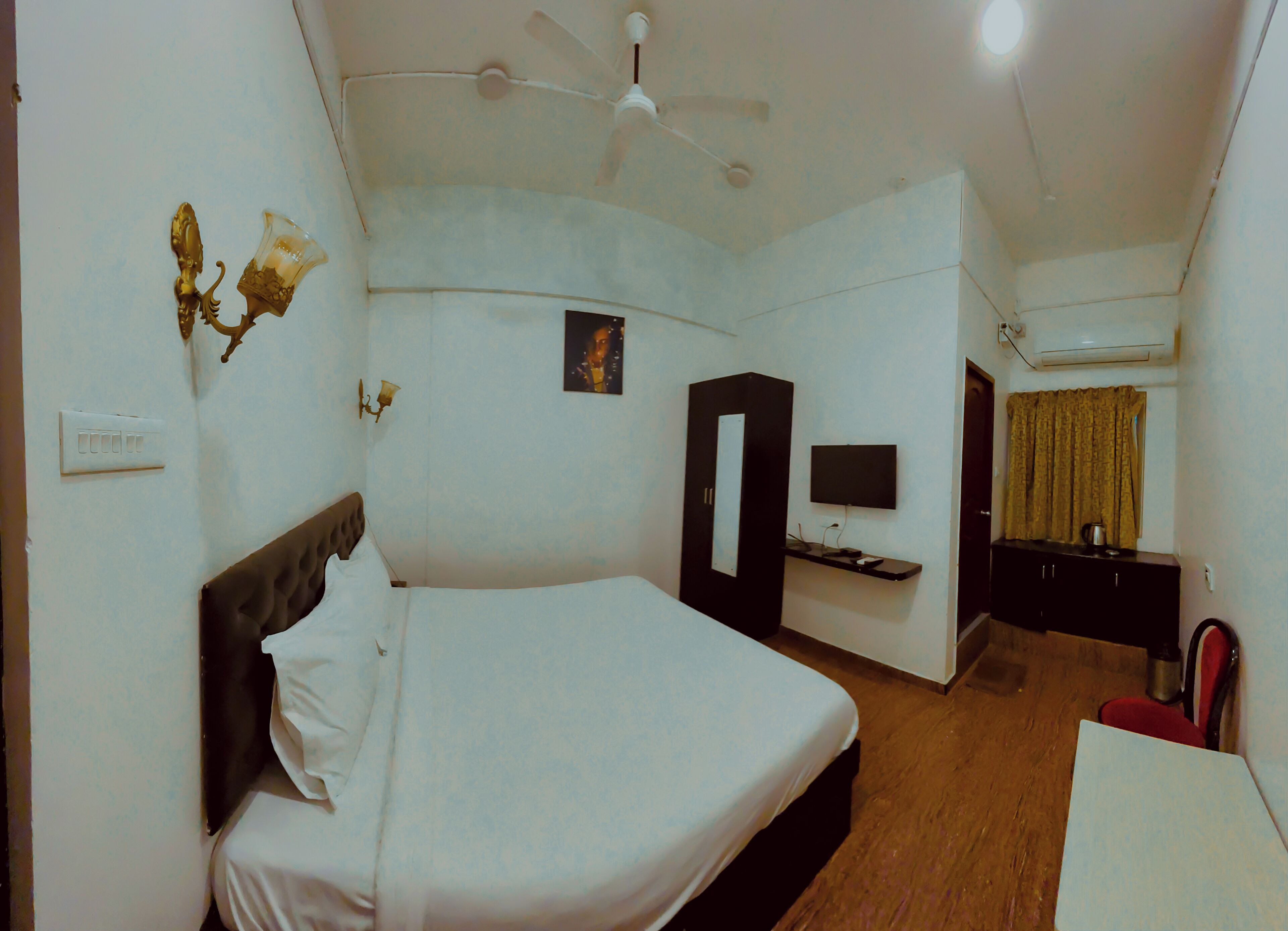 Una habitación de hotel con cama, escritorio, silla, televisor y armario.