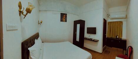 Una habitación de hotel con cama, escritorio, silla, televisor y armario.